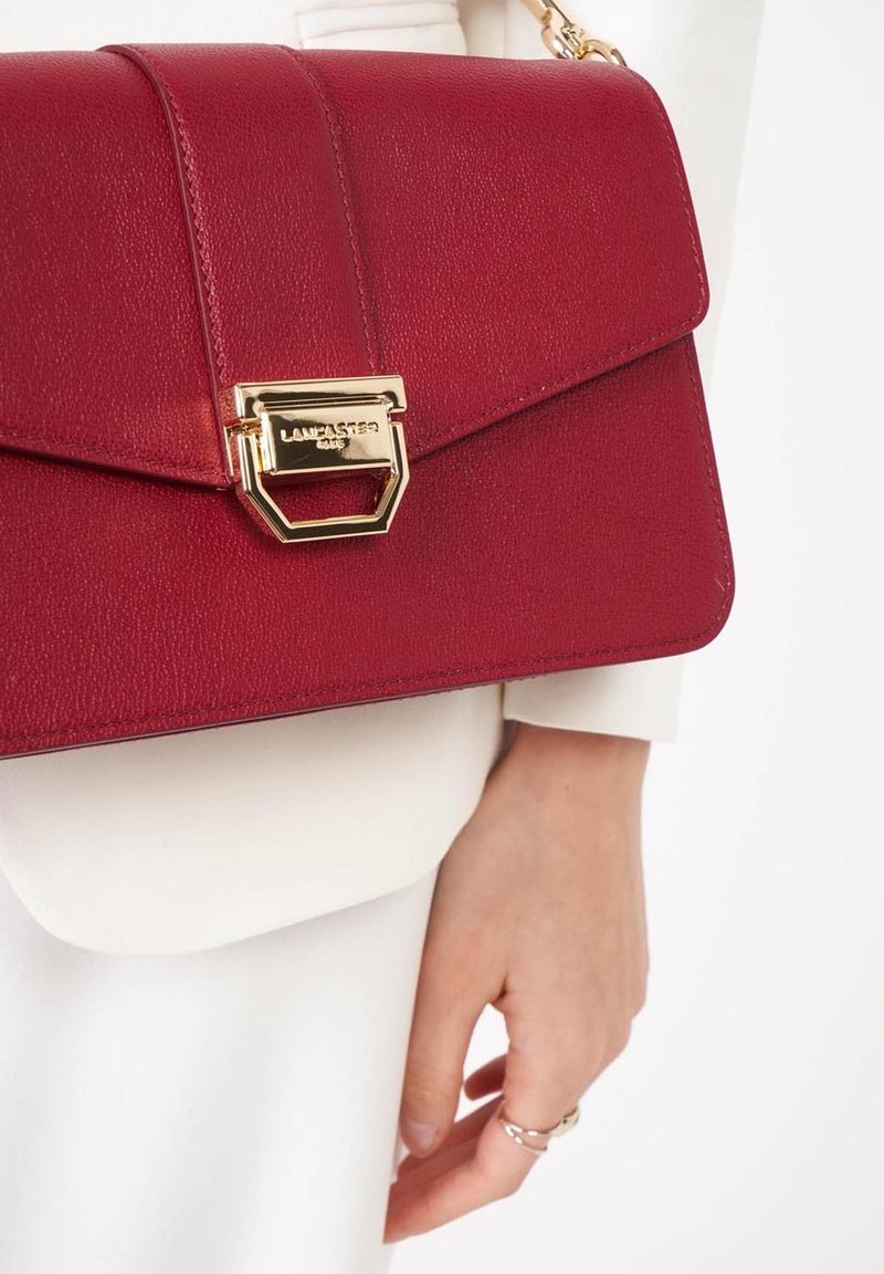 Borsa a mano in pelle rossa con un design strutturato, hardware dorato e chiusura a patta con dettaglio a chiusura geometrica.