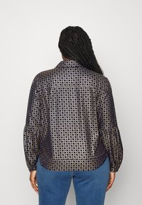 Blusa blu navy con un motivo geometrico dorato, maniche lunghe e colletto, con una vestibilità oversize e una texture di tessuto liscia.