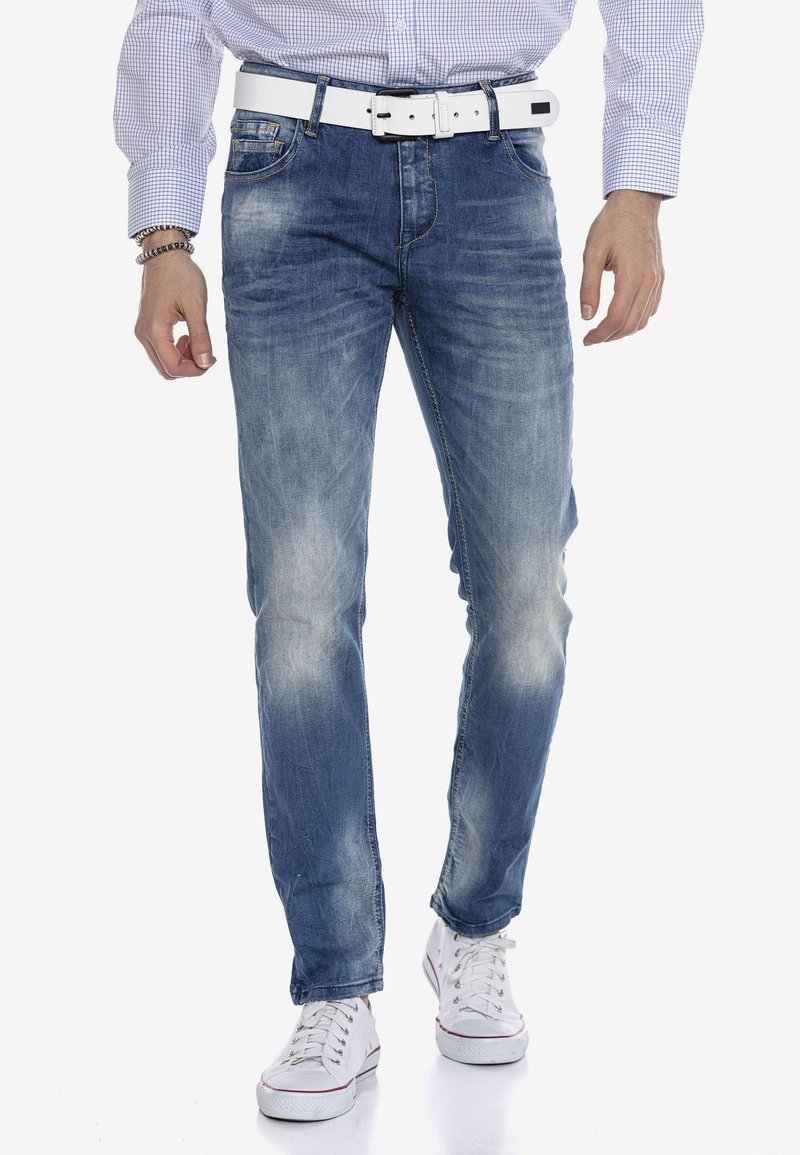 Verblasste blaue Denim-Jeans mit geradem Beinanschnitt, ausgestattet mit fünf Taschen, einem Reißverschluss und einem weißen Gürtel mit quadratischer Schnalle.