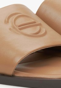 Tan leren instappers met een brede band, een geperst logo-detail en een gladde textuur. Heeft een donkerbruine zool voor contrast.