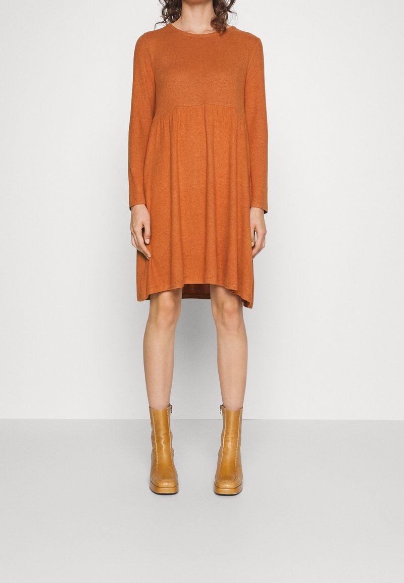 Vestido de punto color óxido con mangas largas, cuerpo ajustado, dobladillo acampanado y textura suave, combinado con botas de tobillo en color beige.