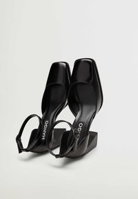 Escarpins en cuir noir à bout carré, à talons hauts blocs avec brides à la cheville, portant la marque "MANGO" imprimée sur la semelle intérieure.