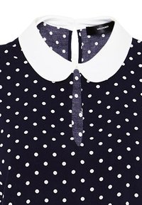 Vestito blu navy con pois bianchi, caratterizzato da un colletto bianco alla Peter Pan e un'apertura a goccia sulla schiena. Tessuto dalla texture liscia.