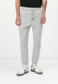 Gray sweatpants with elastic waistband and drawstring, tapered leg design, and side pockets. Paired with white sneakers featuring black accents.