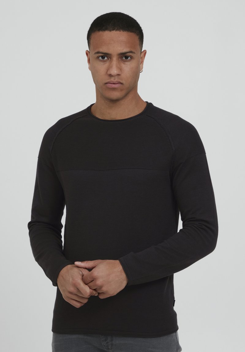 Chemise noire à manches longues avec une texture côtelée et un panneau lisse contrastant sur la poitrine. Encolure ronde, design ajusté.