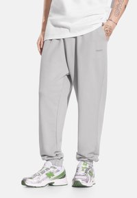 Szare spodnie dresowe wykonane z miękkiego materiału o luźnym kroju, z elastycznymi mankietami i bocznymi kieszeniami, w zestawieniu z metalicznymi sneakersami.