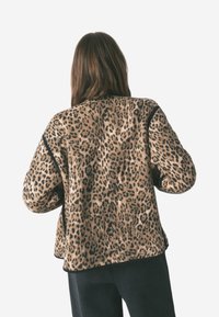 Leopardmønstret jakke i tan og sort, med en afslappet pasform, blød kunstpelsstruktur og kontrasterende sort kant langs sømmene.