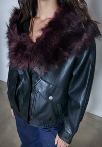 Sort læderjakke med en bred, mørkelilla kunstpelskrave, der har to forlommer og elastisk talje. Glat tekstur.