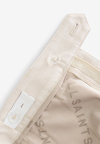 Bézs színű szövet derékpánt átlátszó gombbal, rugalmas szalaggal és „ALLSAINTS” feliratú varrott címkével. Tiszta, sima textúrájú.