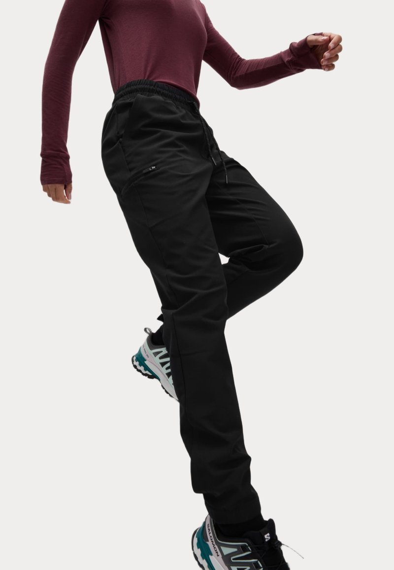 Zwarte sportbroek met een elastische tailleband. Beschikt over ritszakken en een taps toelopende pasvorm. Gecombineerd met zwarte en turquoise trailschoenen.