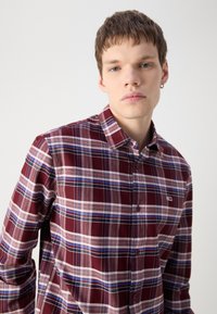Camicia a quadri rossa e blu con colletto button-down, maniche lunghe e una piccola etichetta con logo sul petto. Tessuto di cotone con una superficie liscia.