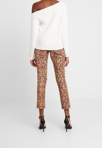 Pull blanc à épaules dénudées en maille côtelée, associé à un pantalon marron moulant à imprimé serpent et des chaussures noires à talons hauts.