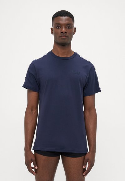T-shirt in cotone blu navy con maniche corte, dotato di collo rotondo e logo goffrato discreto sulla parte anteriore. Dettagli rifiniti lungo le spalle.