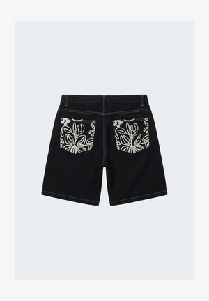 Shorts noirs avec des poches arrière à motif floral blanc et des coutures blanches sur un fond gris clair uni.