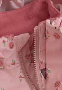Rosa vandtæt jakke med blomstermønster, fleecefor, lynlås og trykknapper. Har et blødt, tekstureret indre for varme.