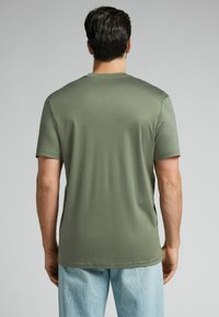 Oliwkowa koszulka z krótkim rękawem o luźnym kroju, gładkiej fakturze i okrągłym dekolcie. Wykończona prostym dołem bez dodatkowych detali.