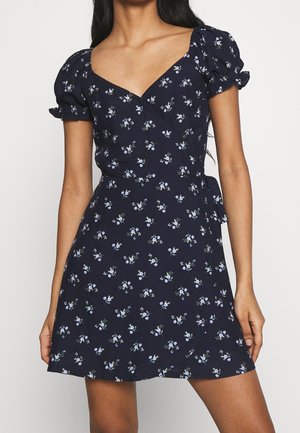 Granatowa sukienka w kwiaty z krótkimi bufkami, dekoltem w serek i dopasowanym gorsetem, ozdobiona rozproszonymi małymi białymi i niebieskimi kwiatowymi wzorami.
