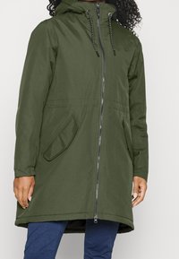 Olivgrön, vattentät parka med huva, framdragkedja och två sidfickor. Har en något avsmalnande silhuett och justerbara dragsko.