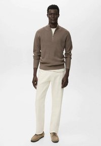 Suéter marrón de canalé con cuello de cremallera, combinado con pantalones color crema. El calzado presenta un diseño de ante beige con un perfil bajo.