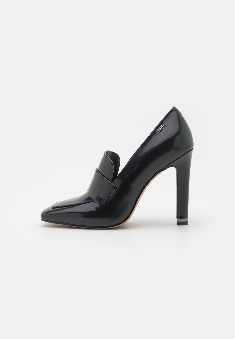 Mocassin noir brillant à talon haut avec bout pointu et détail de bride, doté d’un talon bloc et du logo DKNY près du talon.