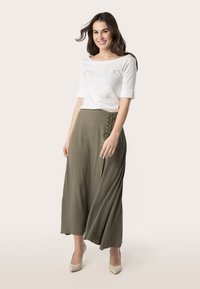 Bílý top s krátkým rukávem zkombinovaný s olivově zelenou maxi suknią s bočním šněrováním. Modelka má na sobě béžové lodičky.