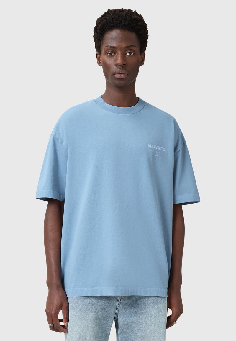 Vaaleansininen puuvillapaita, jossa on rento istuvuus, lyhyet hihat ja pyöreä kaula-aukko. Vasemmassa rinnassa on sävyttä logo.