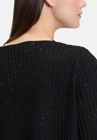 Pull en tricot noir avec une texture côtelée, orné de paillettes argentées sur l'ensemble du tissu. Encolure large et coupe décontractée.