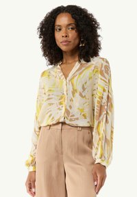 Sheer, long-sleeve blouse with a light abstract pattern in yellow, brown, and white. Features a v-neck and button-down front design.