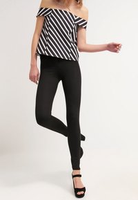 Svarta leggings matchade med en off-the-shoulder topp med djärva svartvita ränder. Toppen har en boxig passform och en texturerad tyg.