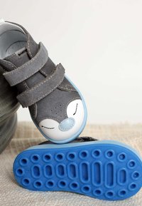 Szare buty na rzep z białym noskiem, ozdobione wzorem twarzy misia. Niebieska gumowa podeszwa z okrągłymi wzorami antypoślizgowymi, teksturowana szara cholewka.