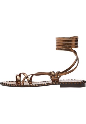 Flache Sandale aus metallisch bronzenem Material mit dünnen, überkreuzten Riemchen und einem umwickelten Knöchelriemen auf einer flachen Sohle mit gesteppten Kanten.
