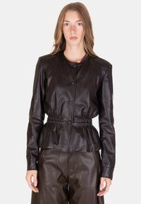 Giacca in pelle marrone con scollo rotondo, chiusura con bottoni e cintura elastica in vita. Texture liscia e vestibilità strutturata, abbinata a pantaloni coordinati.