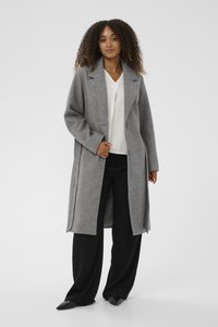 Halli villasegust pikk jakk, lõdva lõikega, krae ja kahe esitnupuga, küljetaskudega, kantud valge särgi ja mustade pükstega.