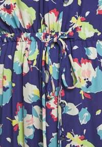 Námořnické šaty s květinovým vzorem v růžové, zelené a bílé. Mají stahovací pás a modré knoflíky vpředu. Hladká textura látky.