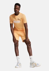 Settimana di abbigliamento attivo con marchio PUMA in morbido colore pesca. Include una maglietta a maniche corte e pantaloni corti, abbinati a calzini bianchi e sneakers.