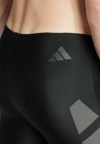 Leggings deportivos negros con una textura suave, que presentan un logo de adidas mate y un diseño de rayas blancas en el costado.