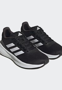 Zapatillas deportivas negras con parte superior de malla, diseño de tres rayas blancas, cordones texturizados, suela acolchada y puntera reforzada.