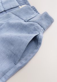Pantalones de mezclilla azul claro con acabado texturizado, con bolsillos laterales y cintura elástica para mayor comodidad. Se puede ver una costura detallada.
