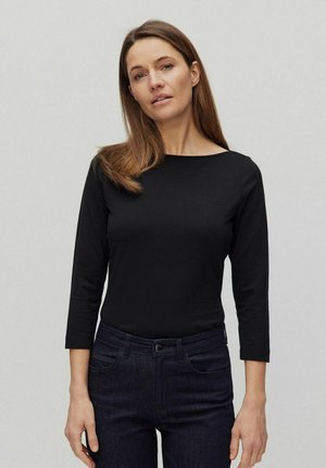 Zwarte lange mouw top met een bateau-nek, gemaakt van zachte stof. Gecombineerd met donkere jeans, met subtiele stiksels en voorzakken.