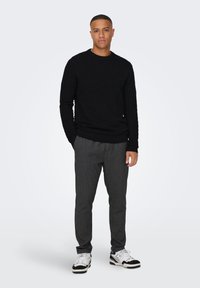 Schwarzer strukturierter Pullover mit Rundhalsausschnitt, kombiniert mit dunkel gestreiften Hosen und weißen Sneakers mit schwarzen Akzenten.