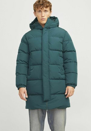Mørkegrøn pufferjakke med lynlås, oversized pasform, lange ærmer og justerbar hætte. Har quiltede syninger og sidelommer.