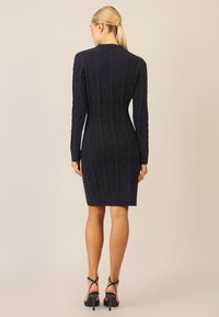Marineblaues gestricktes Kleid mit einem Kabelmuster, langen Ärmeln, taillierter Passform und gerippten Abschlüssen, kombiniert mit schwarzen Riemchen-Heels.