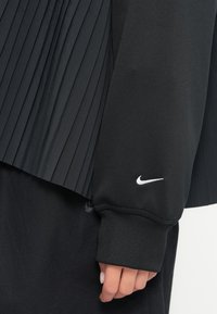 Top atlético preto com um design pregueado, textura suave e um logo branco da Nike na manga. Punhos canelados completam o visual.