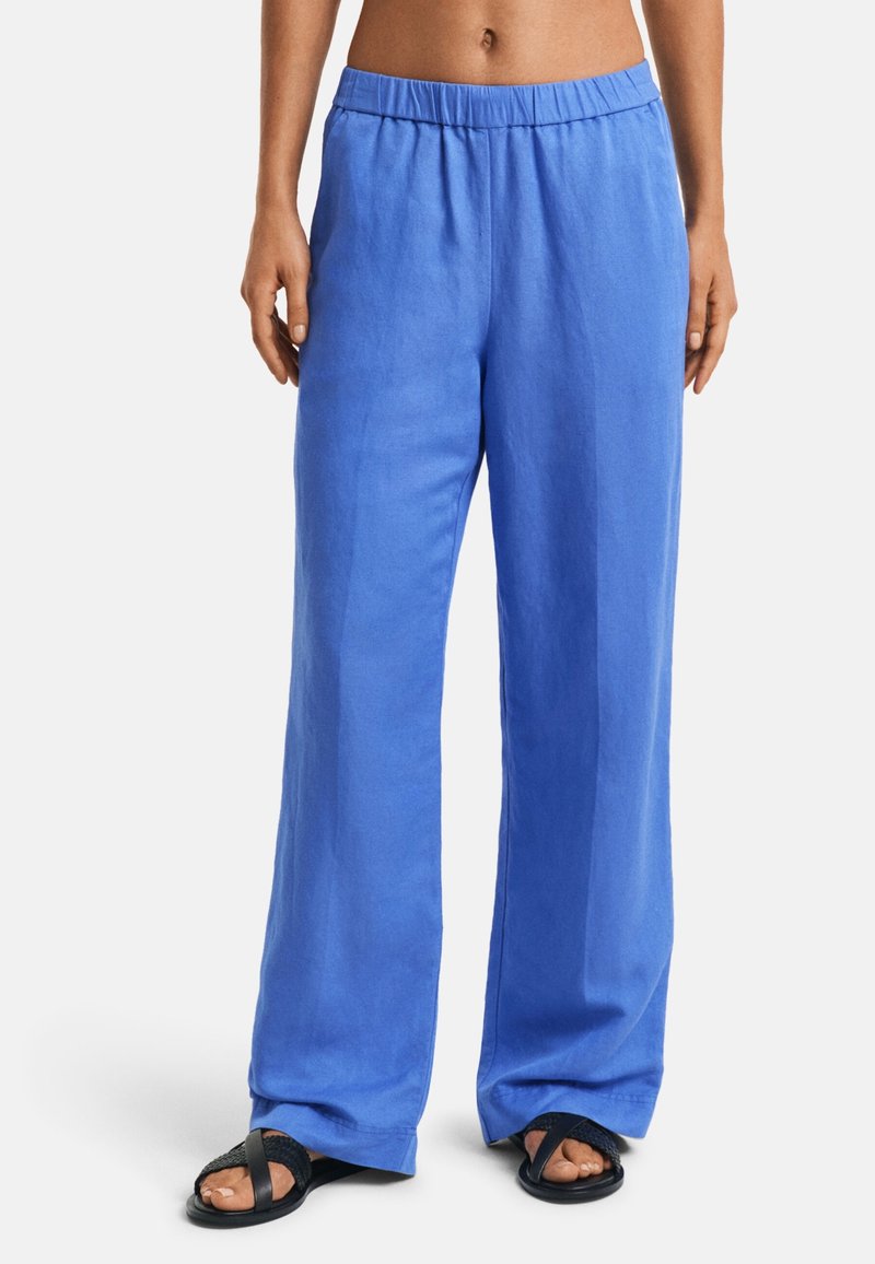 Blue linen wide-leg trousers with an elastic waistband and smooth texture, paired with black slip-on sandals.