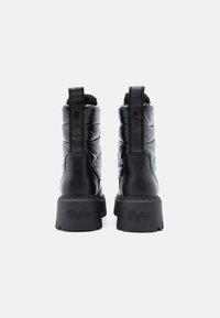 Ζευγάρι μαύρων μονωμένων χειμερινών μπότες με χοντρές σόλες και ταμπέλες επωνυμίας, εμφανιζόμενο από το πίσω μέρος σε λευκό φόντο.