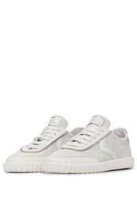 White sneakers with mesh and leather upper, round toe, thin laces, and a textured rubber sole featuring a wave pattern.