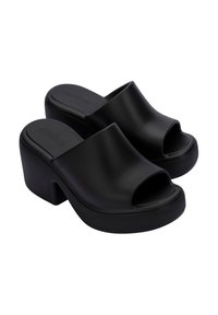 Zuecos de plataforma negros, fabricados en material sintético suave, con un diseño de punta abierta y un tacón curvado para mayor altura y comodidad.