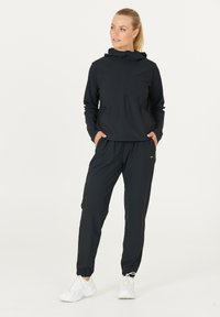 Schwarzes Sport-Set mit einer Zip-Hoodie-Jacke in lockerer Passform und elastischen Bündchen, kombiniert mit tapered Jogginghosen und weißen Sneakers.