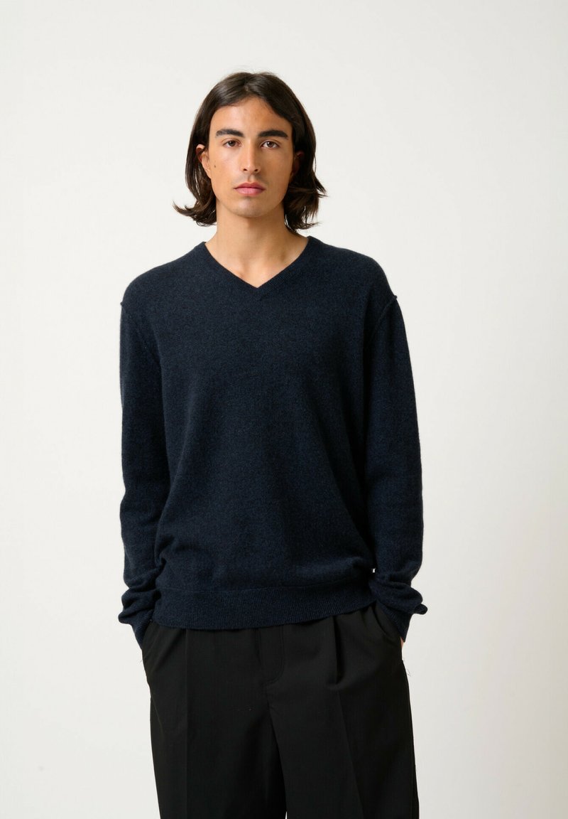 Suéter azul marino de cuello en V hecho de una tela suave, con mangas largas y un corte relajado, combinado con pantalones negros.