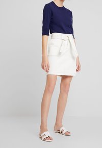 Tmavě modrý pletený top s kulatým výstřihem a krajkovým lemováním; bílá džínová sukně s páskem na zavázání, s kapsami a detaily prošívání; bílé nazouváky.